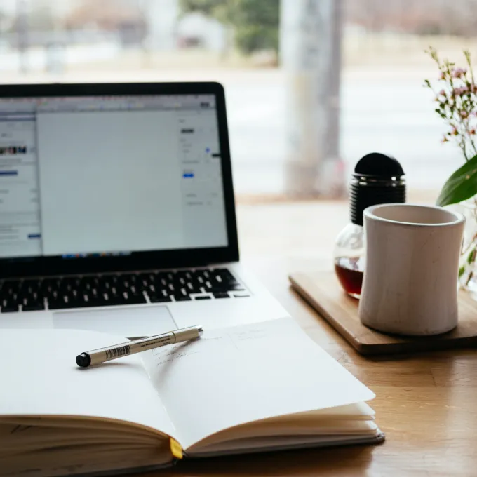 notebook laying open on a table with laptop on in the background